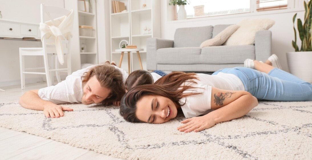 Happy family lying on a freshly cleaned, soft rug in a bright and cozy living room.