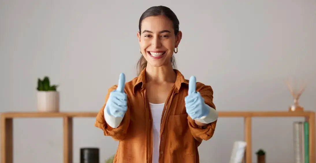 Smiling woman wearing cleaning gloves giving a thumbs-up, showing satisfaction with a clean and organized home.