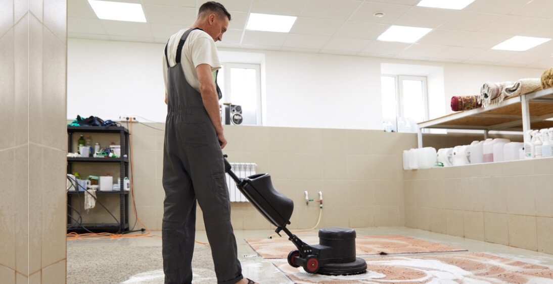 Professional cleaner using an industrial machine to deep clean a large rug in a specialized cleaning facility.